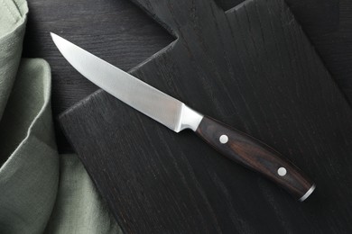 One sharp knife, cloth and board on black wooden table, top view