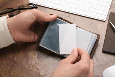 Man holding leather business card holder with blank cards at wooden table, closeup