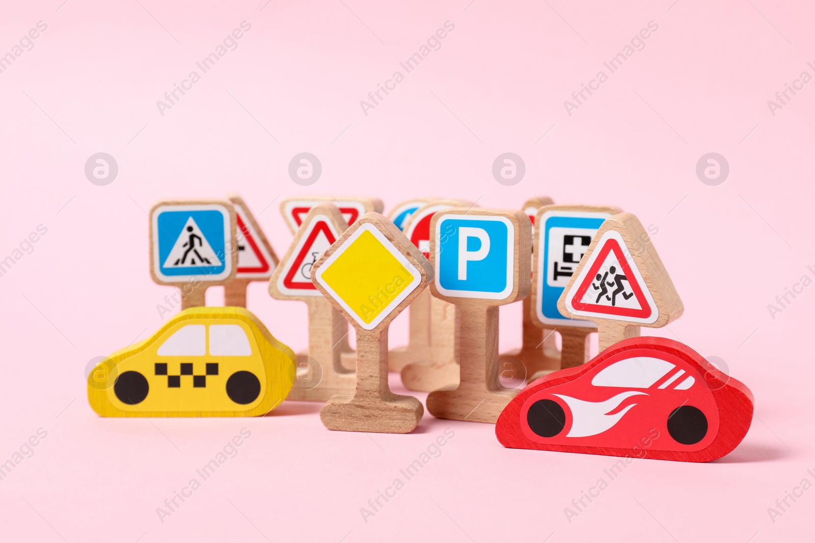Photo of Set of wooden road signs and cars on light pink background. Children's toy