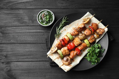 Photo of Delicious shish kebabs with vegetables served on black wooden table, flat lay. Space for text