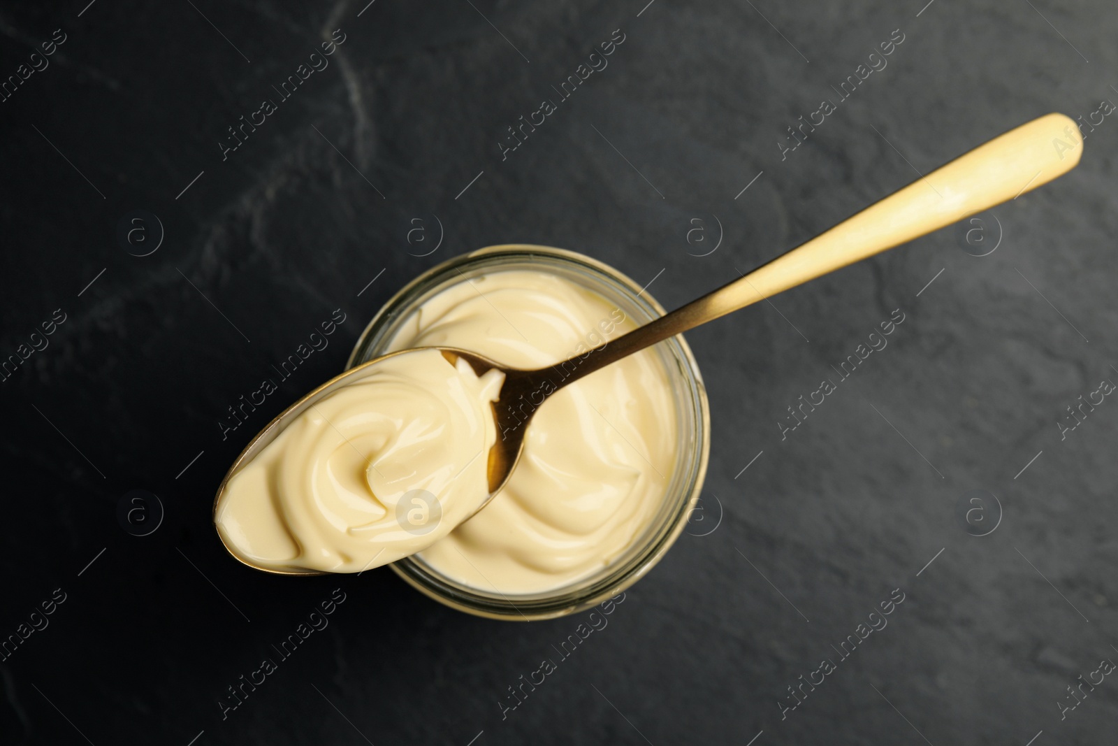 Photo of Jar of delicious mayonnaise and spoon on black table, top view