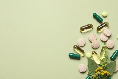 Different pills and herbs on light green background, flat lay with space for text. Dietary supplements