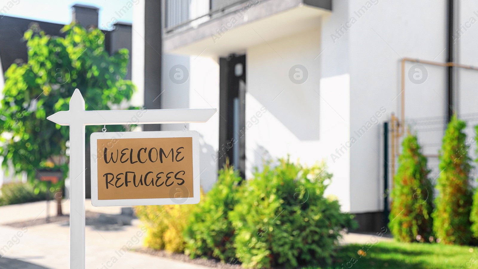 Image of Sign with phrase WELCOME REFUGEES near house outdoors on sunny day