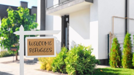 Image of Sign with phrase WELCOME REFUGEES near house outdoors on sunny day