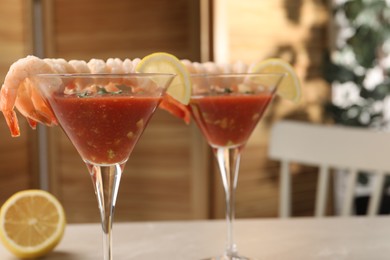 Tasty shrimp cocktail with sauce in glasses and lemon on light table, space for text