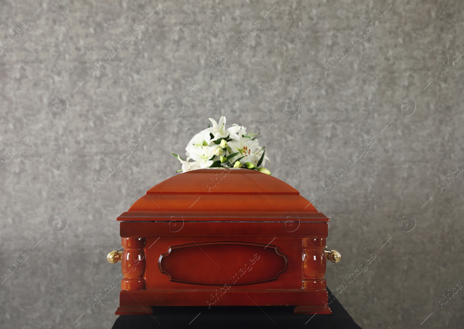 Photo of Wooden funeral casket with white lilies at grey wall