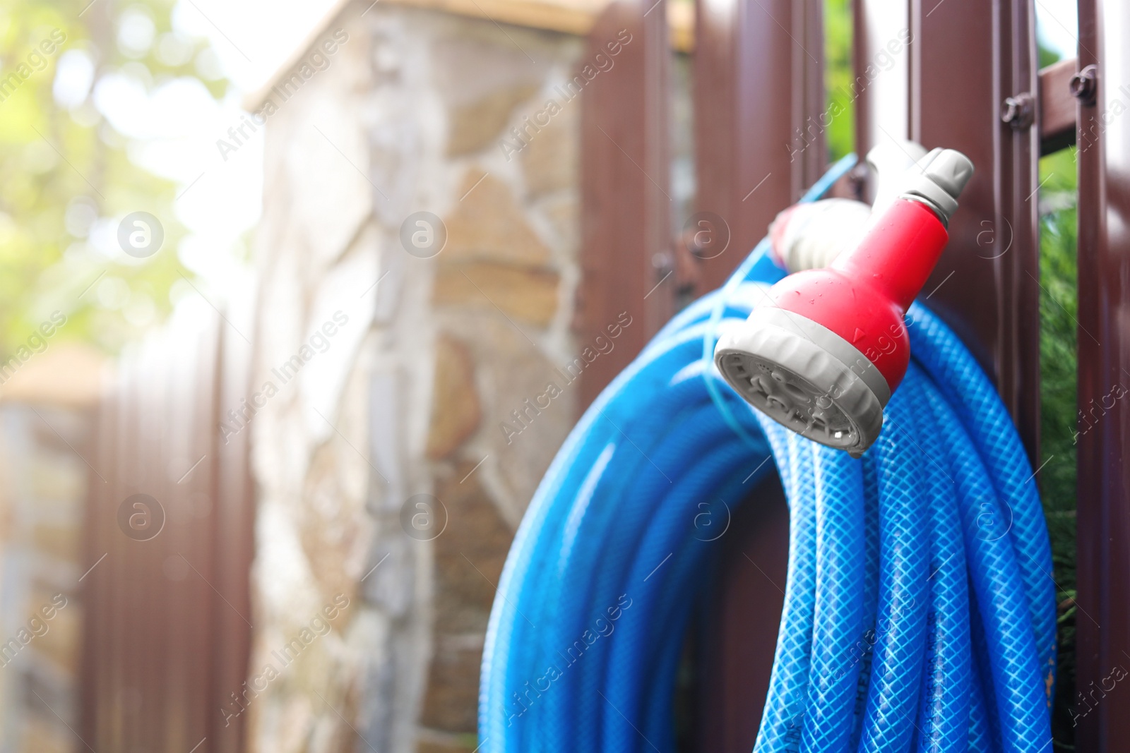 Photo of Watering hose with sprinkler hanging on wooden fence in garden, closeup. Space for text