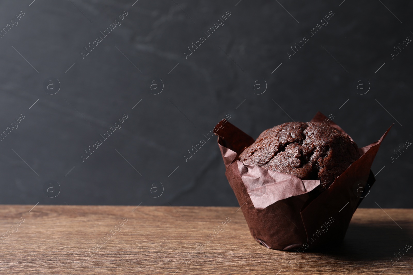 Photo of Tasty chocolate muffin on wooden table, closeup. Space for text