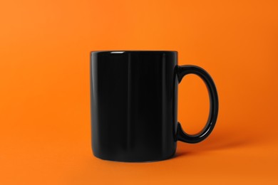 Photo of One black ceramic mug on orange background