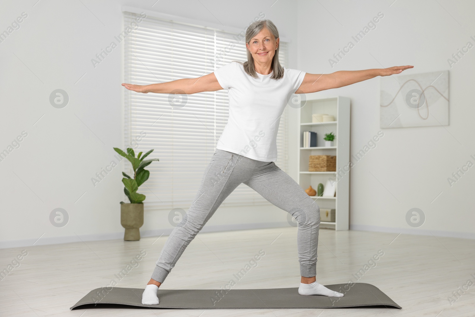 Photo of Happy senior woman practicing yoga on mat at home