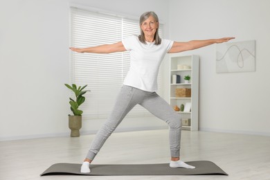 Happy senior woman practicing yoga on mat at home