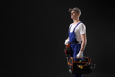 Professional repairman with tool box on black background. Space for text