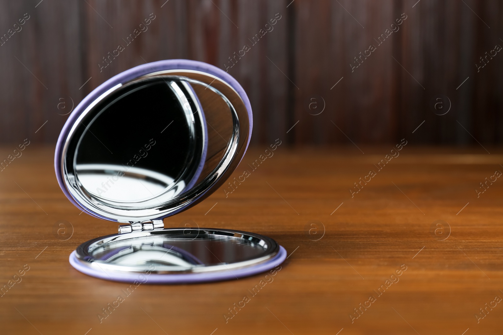 Photo of Stylish cosmetic pocket mirror on wooden table. Space for text