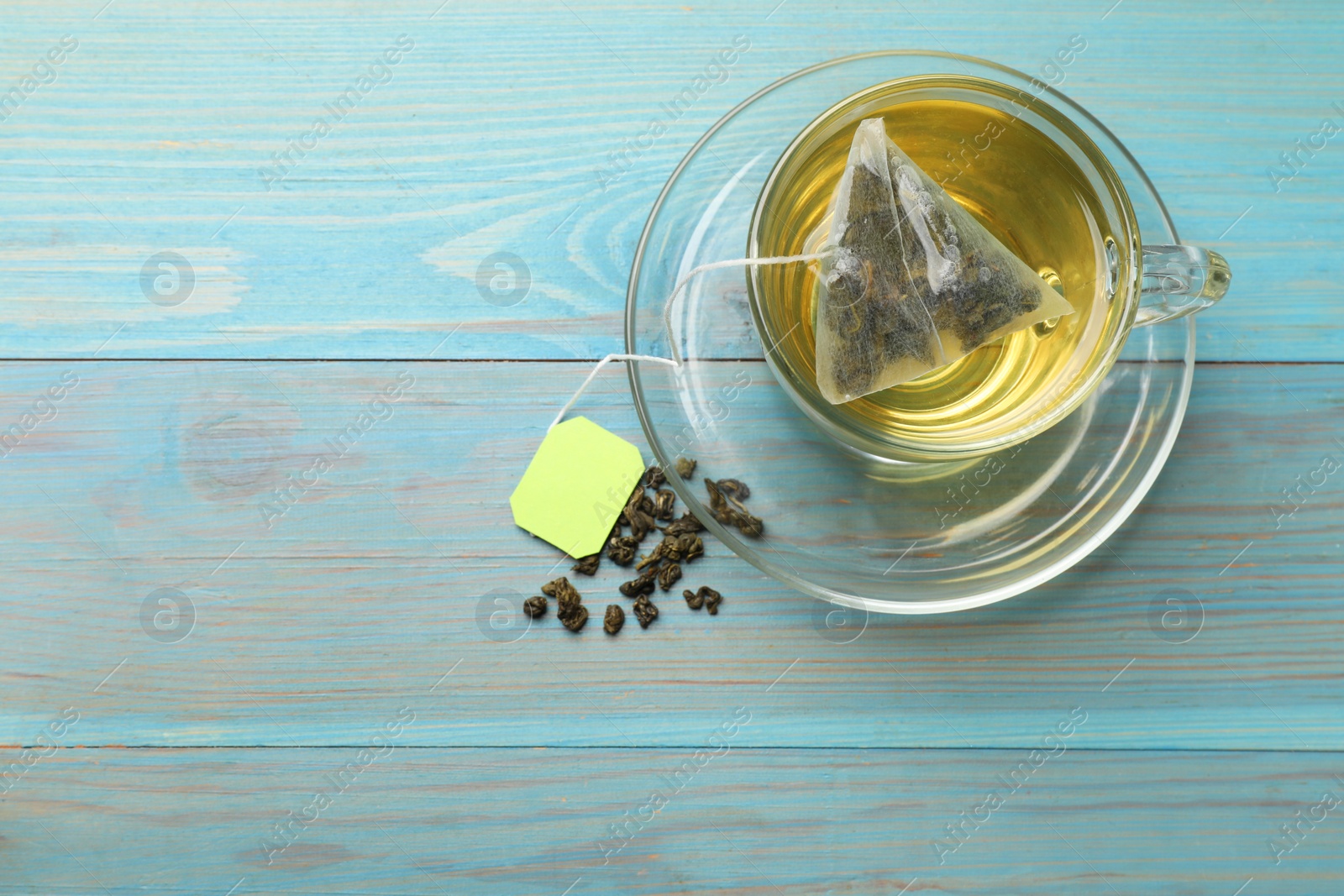 Photo of Tea bag in cup with hot drink and dry leaves on light blue wooden table, top view. Space for text
