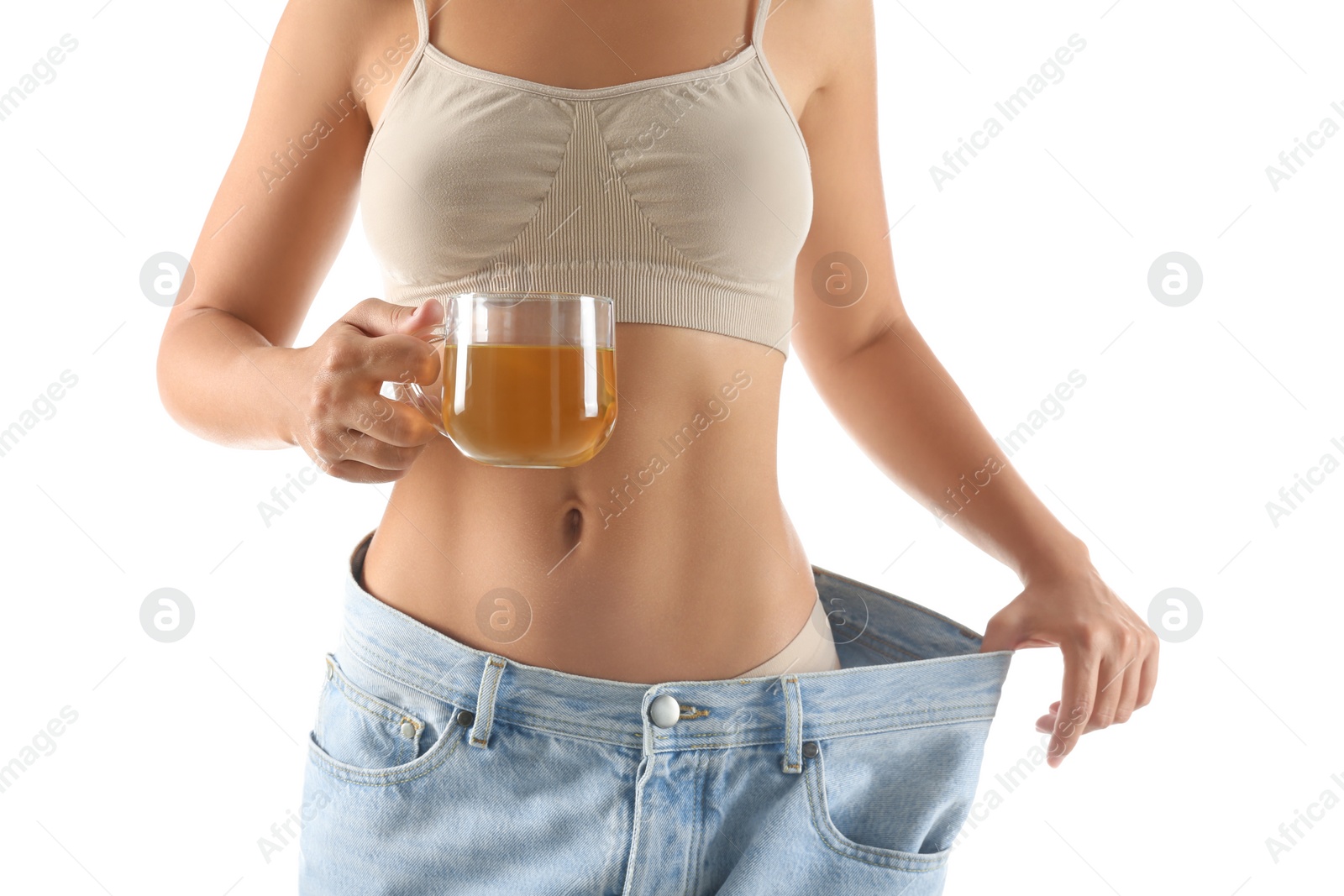 Photo of Young woman in old big jeans with cup of tea showing her diet results on white background, closeup