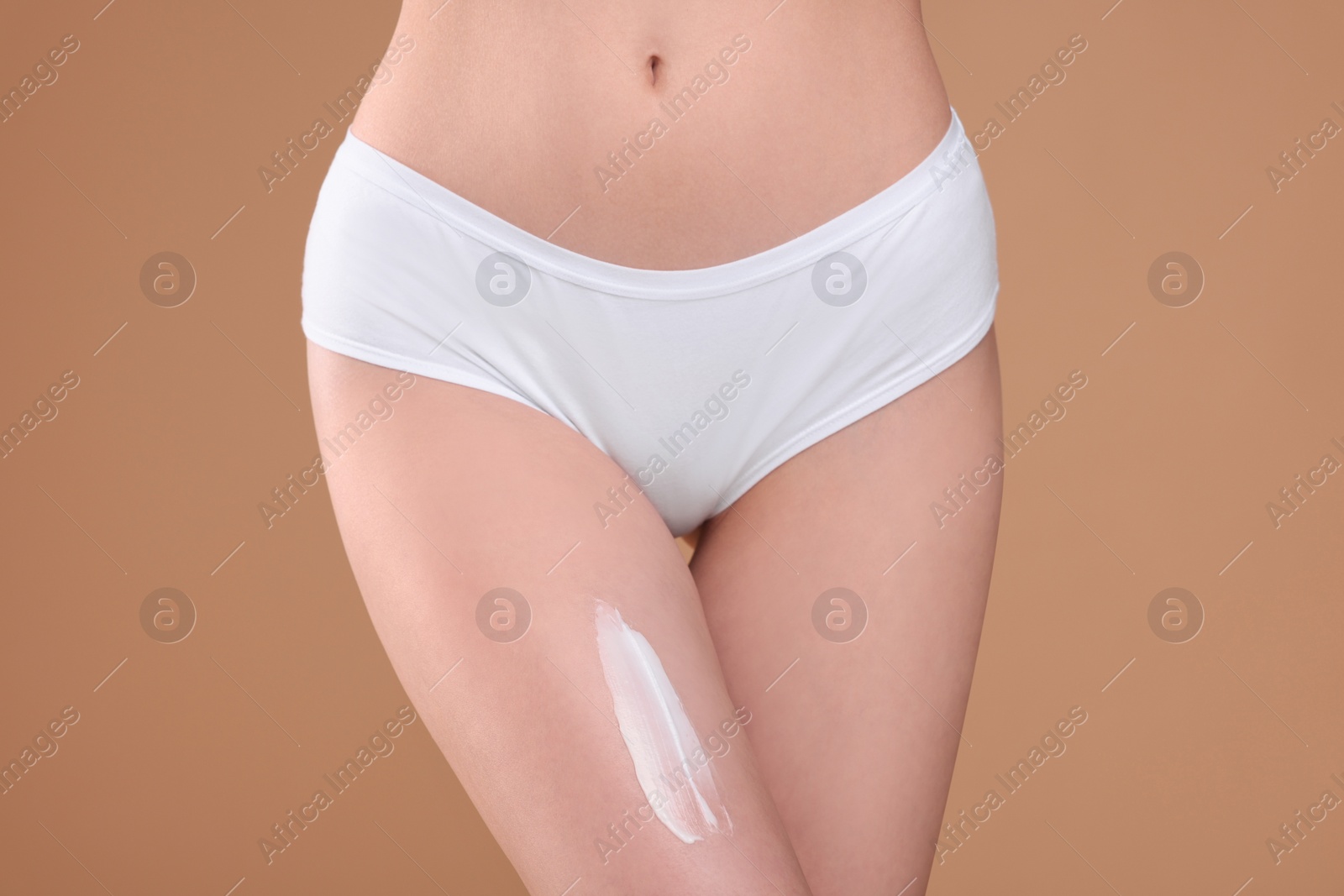 Photo of Woman with smear of body cream on her leg against light brown background, closeup