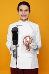 Chef holding sous vide cooker and meat in vacuum pack on orange background