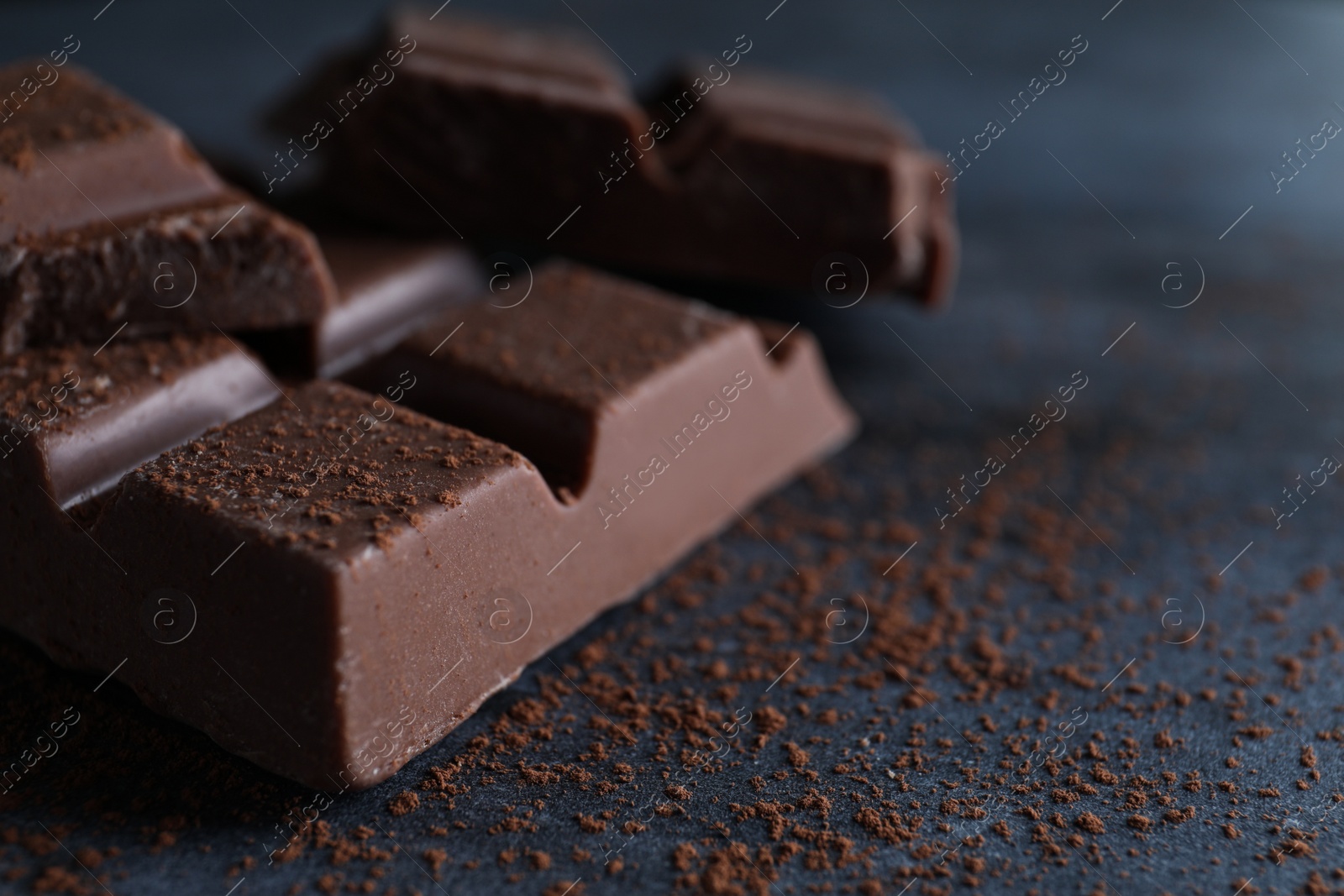 Photo of Delicious milk chocolate and cocoa powder on black table, closeup