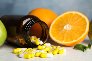 Bottle with vitamin pills and fruits on white table, closeup