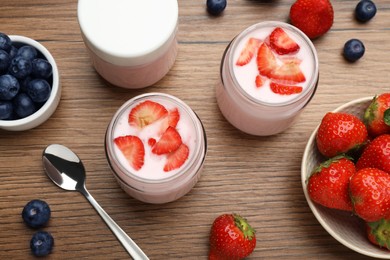 Jars of fresh yogurt, strawberry and blueberry on wooden table, flat lay