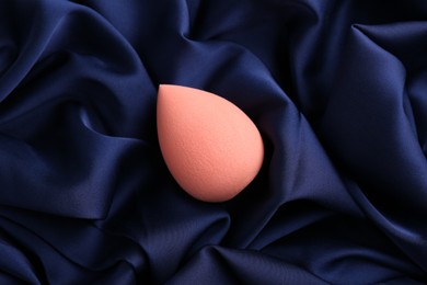 Photo of Beige makeup sponge on blue silk cloth, top view