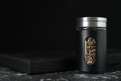 Photo of Pepper shaker on dark table against black background. Space for text