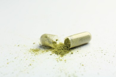 Photo of Broken light green vitamin capsule on white background, closeup