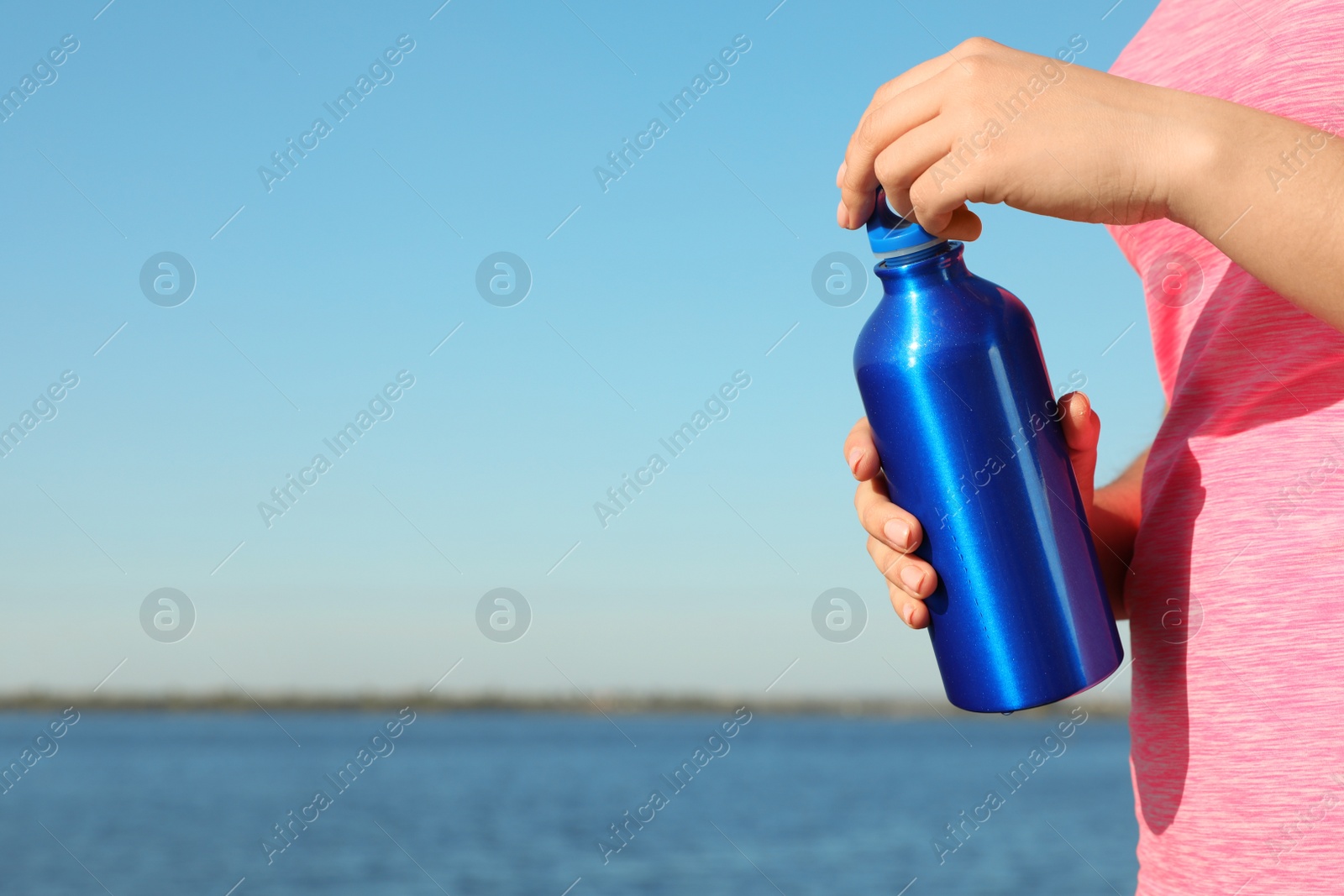 Photo of Young sporty woman with water bottle outdoors on sunny day, closeup. Space for text