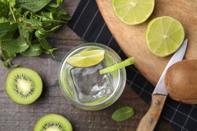 Photo of Glass of refreshing drink with cut kiwi and lime on wooden table, flat lay