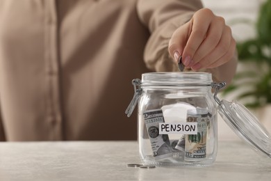 Photo of Pension savings. Woman putting coin into glass jar with money at light table, closeup