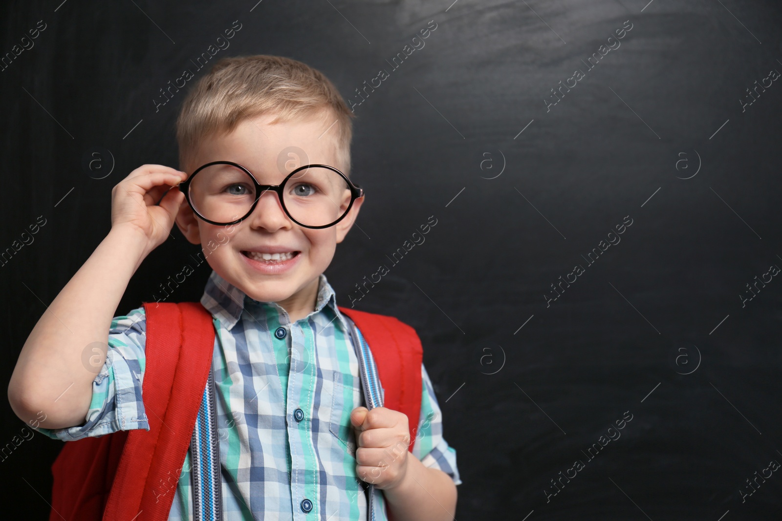 Photo of Cute little child wearing glasses near chalkboard, space for text. First time at school