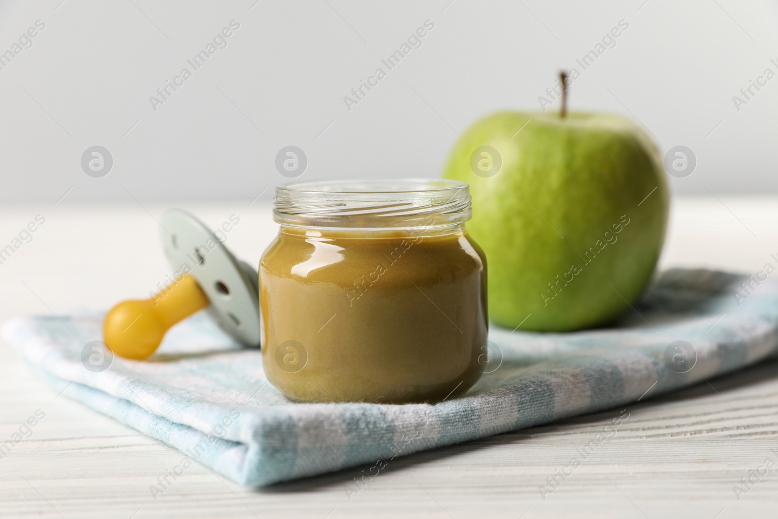 Photo of Jar with healthy baby food, apple and pacifier on white wooden table