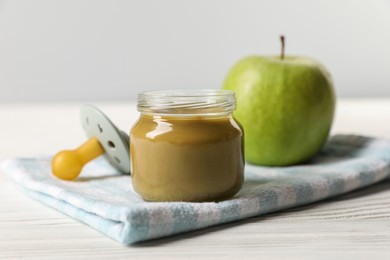 Photo of Jar with healthy baby food, apple and pacifier on white wooden table