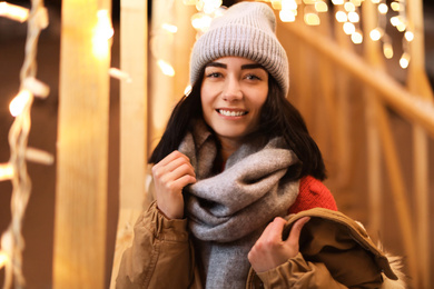 Beautiful young woman near festive lights outdoors. Winter vacation