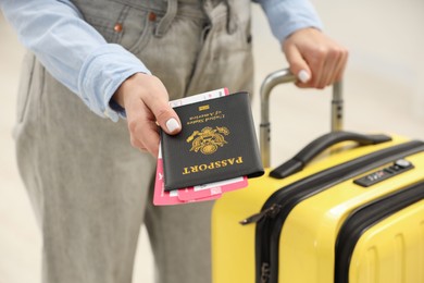 Photo of Woman with suitcase giving passport and tickets on blurred background, closeup