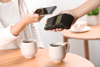 Woman using terminal for contactless payment with smartphone in cafe