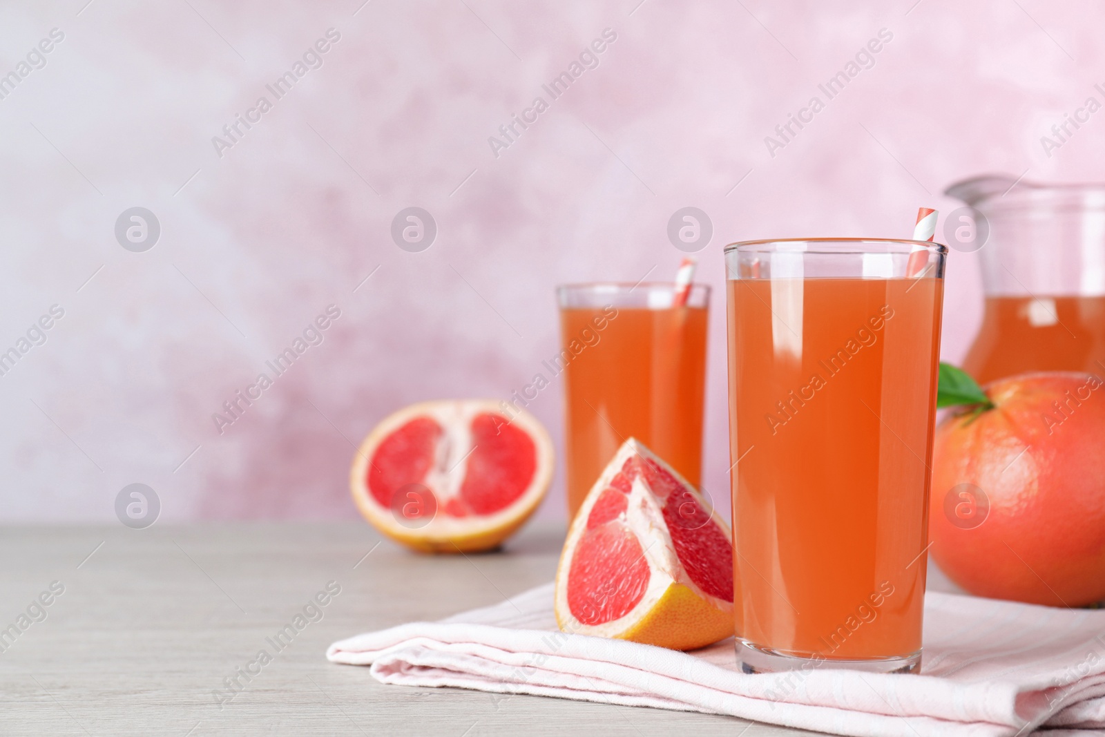 Photo of Tasty freshly made grapefruit juice on white wooden table. Space for text