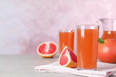 Photo of Tasty freshly made grapefruit juice on white wooden table. Space for text