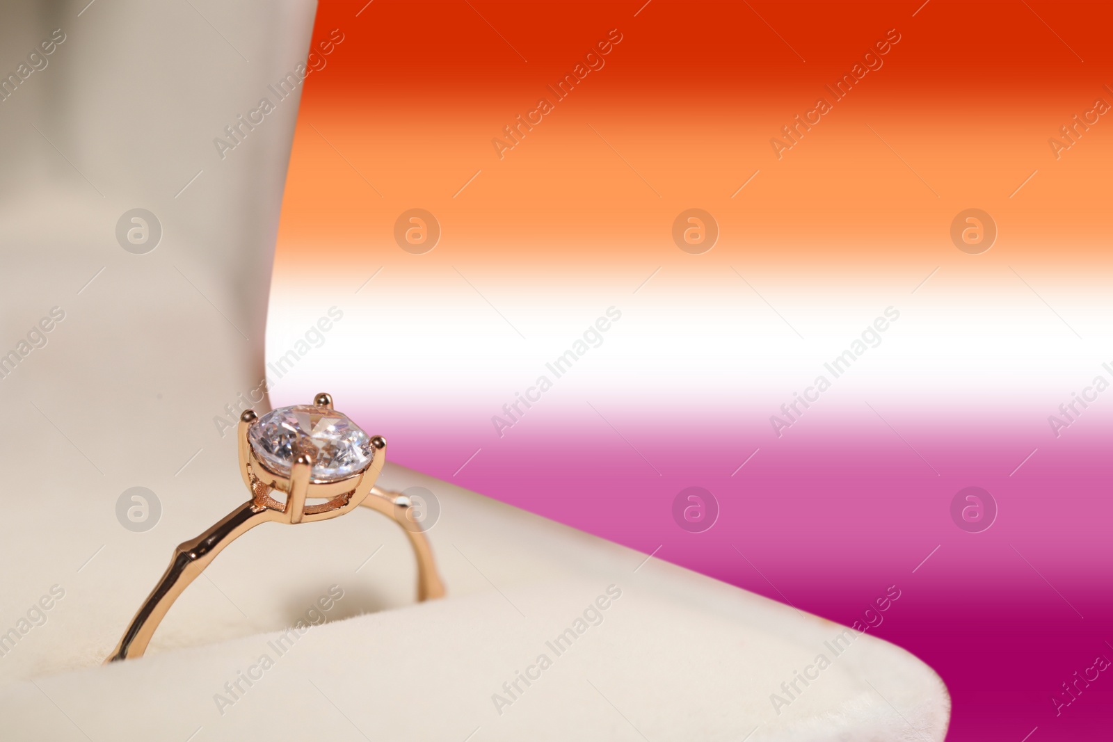 Image of Box with beautiful engagement ring on background in color of lesbian flag, closeup