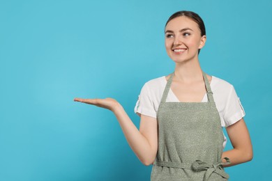 Photo of Beautiful young woman in clean apron with pattern on light blue background. Space for text