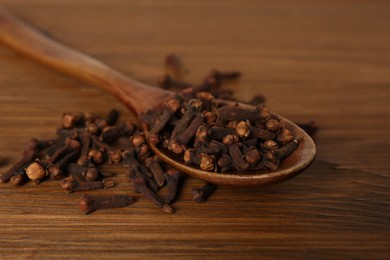 Aromatic dry cloves and spoon on wooden table, closeup
