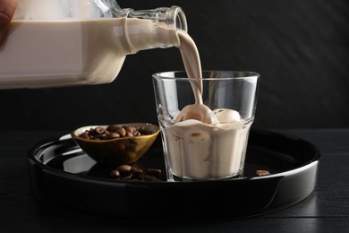 Pouring coffee cream liqueur into glass at black wooden table, closeup