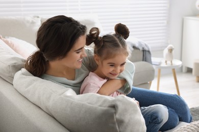 Photo of Young mother and her daughter spending time together on sofa at home