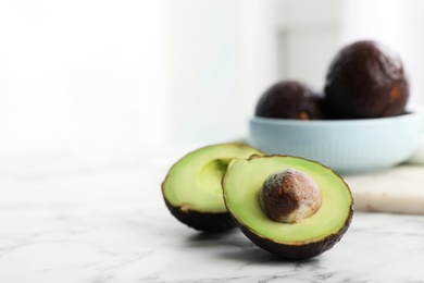 Photo of Halves of delicious ripe avocado on white marble table against light background