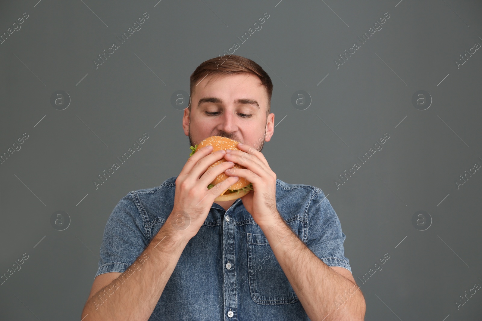 Photo of Young man eating tasty burger on grey background