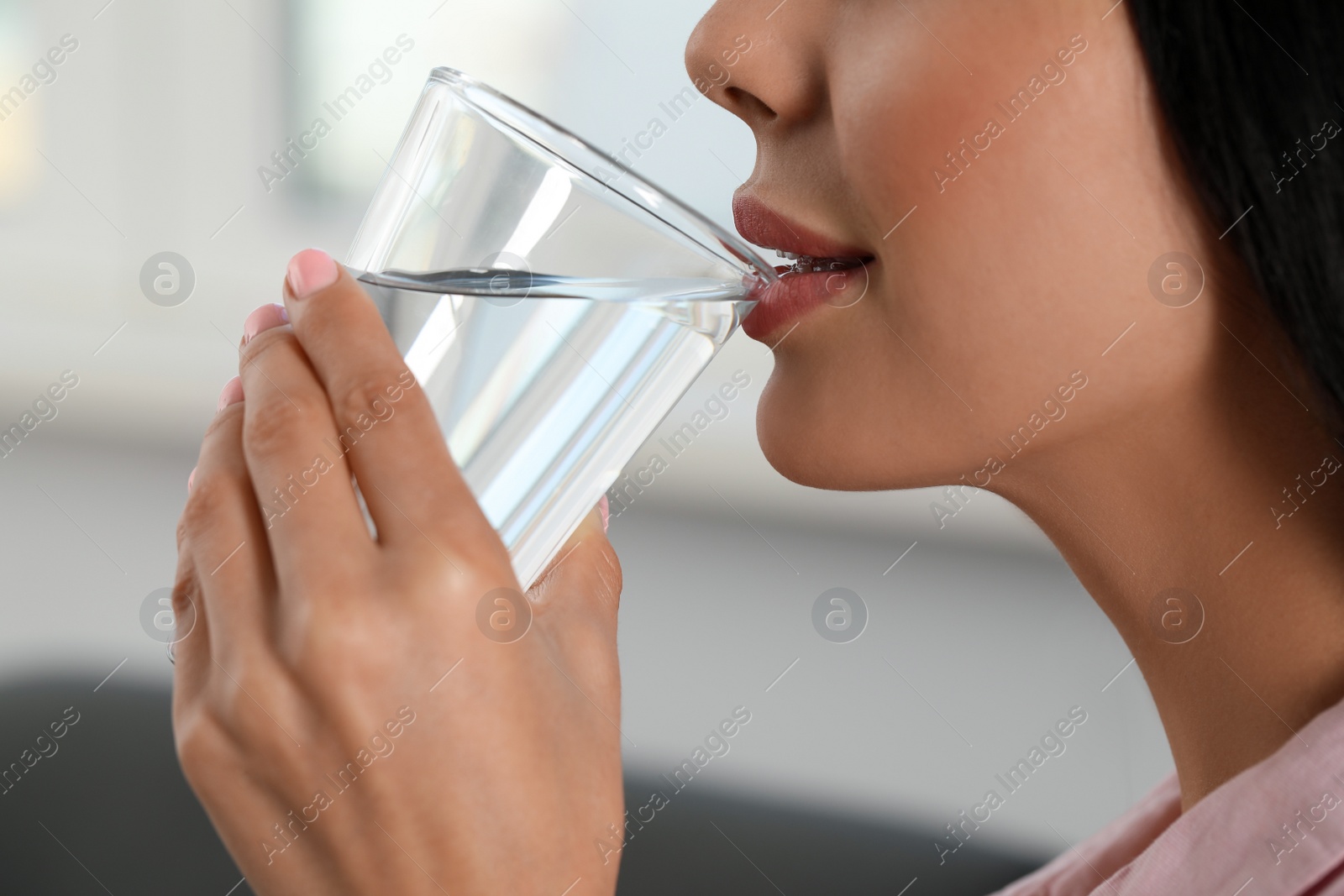 Photo of Young woman drinking water indoors, closeup. Refreshing drink