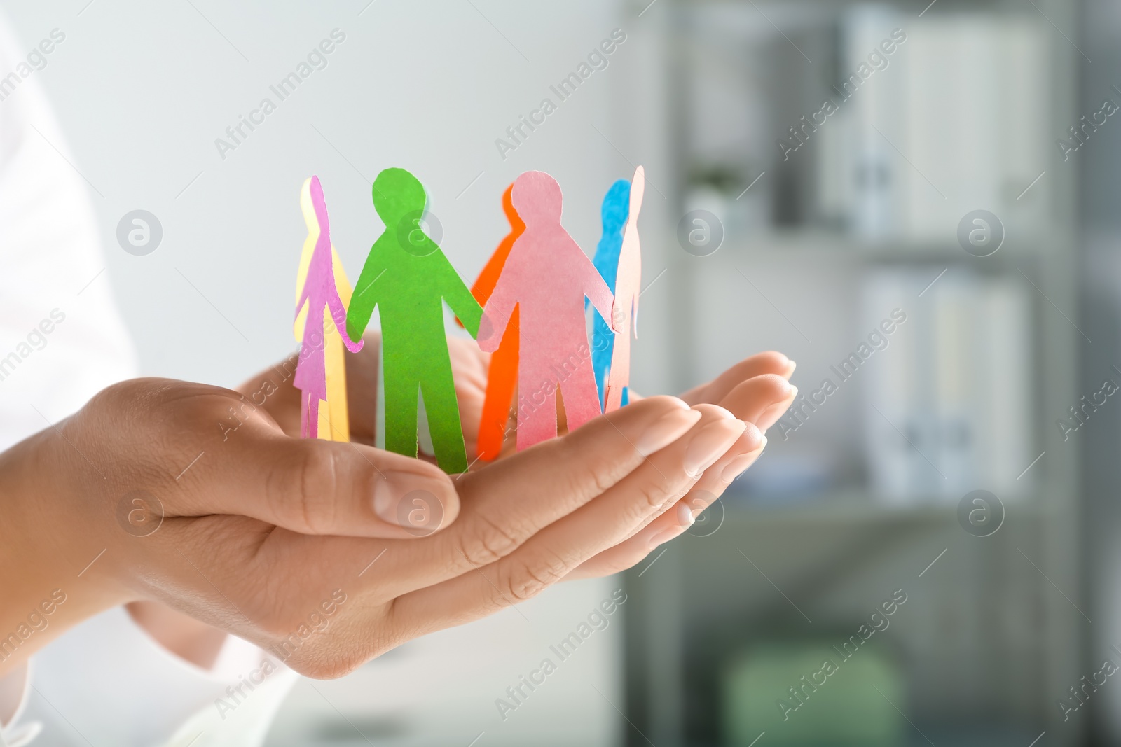 Photo of Woman holding paper human figures on blurred background, closeup. Diversity and inclusion concept