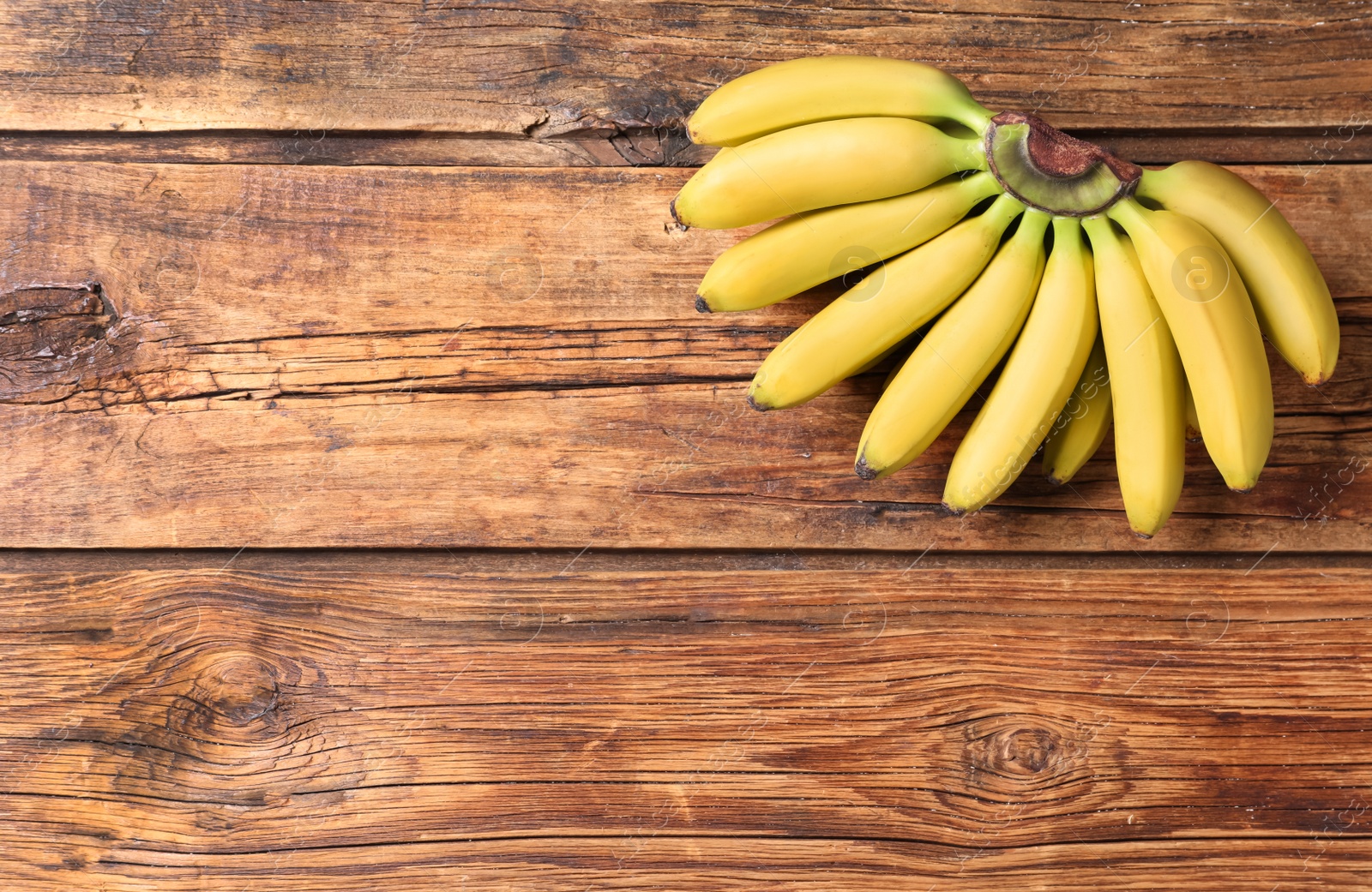 Photo of Bunch of ripe baby bananas on wooden table, top view. Space for text