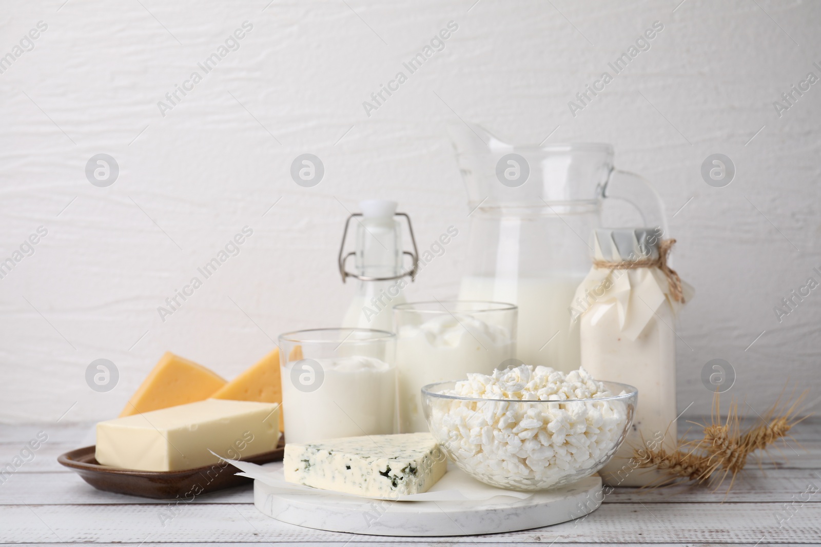 Photo of Different fresh dairy products and wheat ears on white wooden table