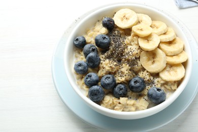 Photo of Tasty oatmeal with banana, blueberries and chia seeds served in bowl on white wooden table, space for text